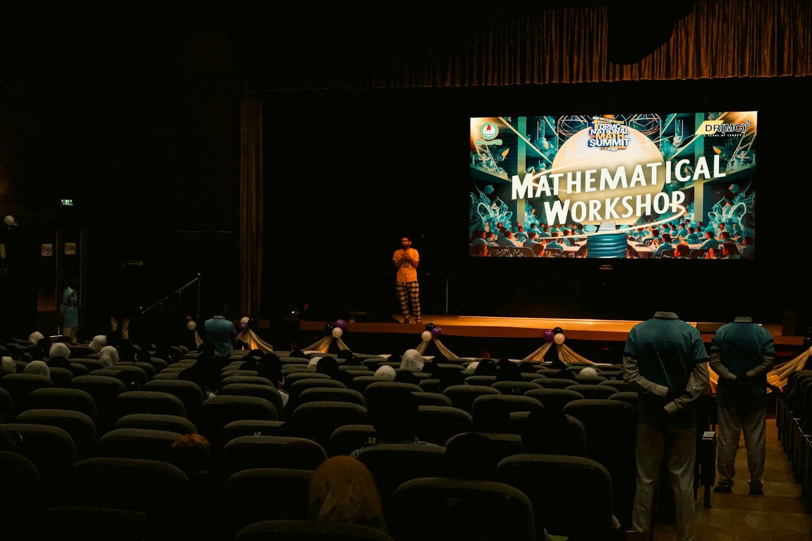 A speaker on stage presenting a workshop to an audience